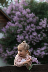 Spring flowering. Portrait of a beautiful little girl 3 years old with lilac flowers in nature. Childhood. The kid poses, but does not look at the camera.