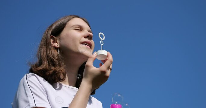 The girl blows soap bubbles against the background of the blue sky.