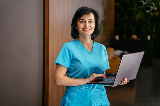 Portrait Of Attractive Middle Age Female Hispanic Woman Doctor Psychiatrist Or Therapist Wearing Uniform Using Laptop In Hospital Clinic Office.