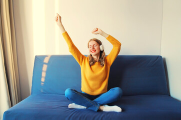 Happy cheerful young woman listening to music with wireless headphones having fun sitting on the couch at home