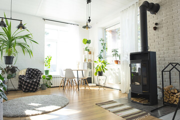 The interior of the house with large windows and home plants round table, metal stove fireplace,...