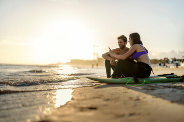 Surfers sitting on a beach and smiling at the phone.