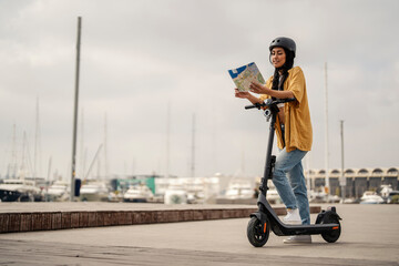 An urban tourist is standing on an eco friendly electric scooter and looking at the city map while...