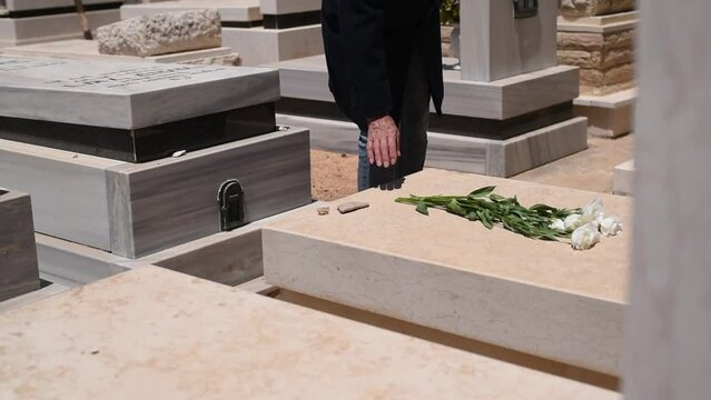 Gravestones and graves at jewish  cemetery. Person bring flowers to lost in Israel at the outskirts of Tel Aviv. Hebrew texts note the names and details of the deceased. Monuments by back side