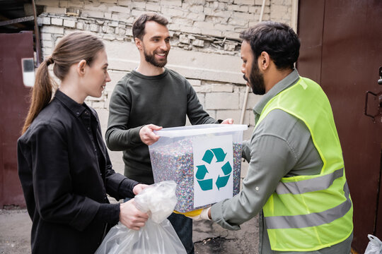 Smiling volunteers giving trash to indian worker in high visibility vest in outdoor waste disposal station, garbage sorting and recycling concept