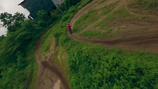 Extreme motocross track moto riding male speed race on winding sand dirt path at tropical jingle countryside aerial view. FPV sport drone motorbike speed adrenaline ride offroad trail exotic scenery