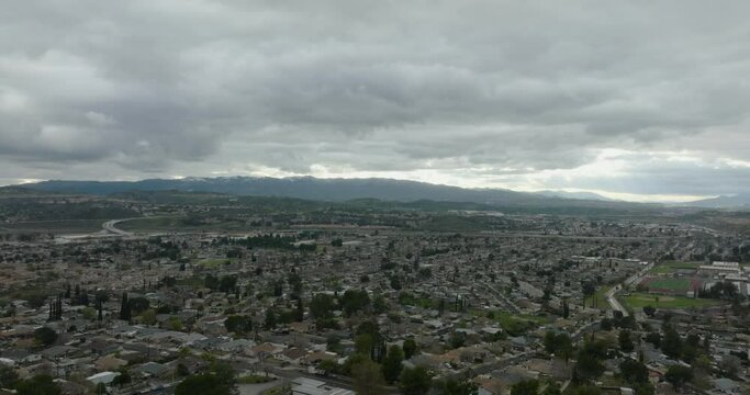 Santa Clarita, California seen in this wide aerial view of hundreds of suburban tract homes on a winter day with looming storm clouds and snowy covered hills in the background.