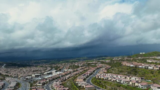Aerial timelapse of suburban tract homes along a hillside in Santa Clarita, California as winter storm clouds pass overhead and cast a shadow on the homes below.