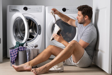 Man doing laundry at home near washing machine. Husband man doing laundry at home. Sexy guy washer putting clothes in the washing machine. Household concept. Washer and dryer, laundromat. - Powered by Adobe
