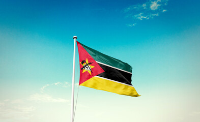 Waving Flag of Mozambique in Blue Sky. The symbol of the state on wavy cotton fabric.