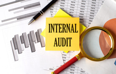 INTERNAL AUDIT text on a sticky on the graph background with pen and magnifier