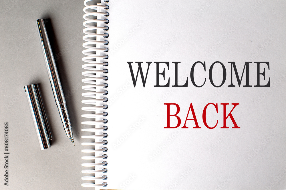 Aufkleber welcome back text on a notebook with pen on grey background