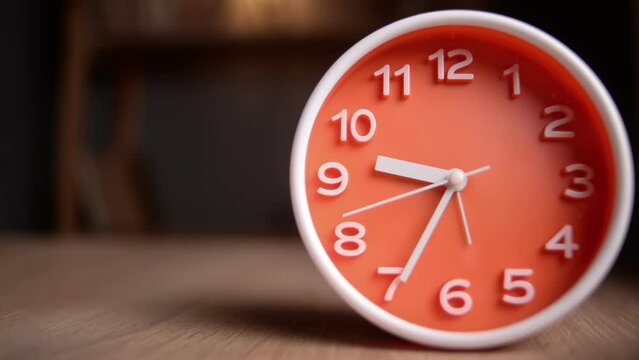 Time lapse of a orange clock on table. The clock starts ticking at 9 and ends at 10.beautiful alarm clock face. Stop motion animation of alarm clock running.