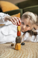 Wooden blocks. 
A girl plays with wooden balancing cubes. Educational games for children. Wooden blocks in shapes of gems of various colours. The girl builds a pyramid from wooden blocks.