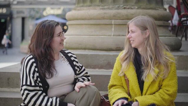 Two females sitting on steps chatting and enjoying each other's company