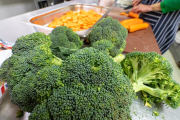 Broccoli florets in a pil with carrots in the background, ready for cooking. Brocolli plant is in the cabbage family.