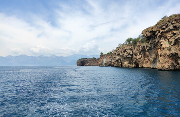 Obraz premium Blue Mediterranean sea, blue sky with white clouds and a rocky shore with a cliff