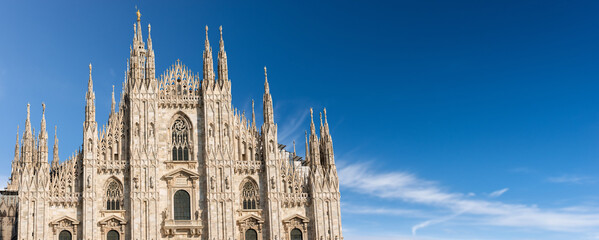 Fototapeta premium Facade of the Duomo di Milano against a clear blue sky with clouds and copy space. (Milan Cathedral 1418-1577). Church, monument symbol of Lombardy, Italy, Europe. 