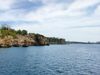 Fototapeta premium Blue Mediterranean sea, blue sky with white clouds and a rocky shore with a cliff