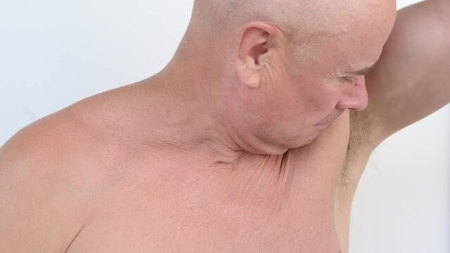european mature man, senior 60 years old with naked torso carefully examines, checks armpits for smell of sweat, regulation of perspiration, fight against unpleasant odor, smell of old age