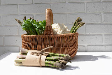 Healthy food background. A fresh asparagus and green basilica in a straw basket on white wooden table. Front view