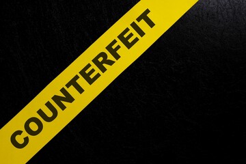 Counterfeit product and item caution and warning concept. Yellow barricade tape with word in dark...