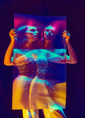 Fashion model, young girl wearing trendy clothes posing over violet background in neon light. Blurred effect. Mirror reflection