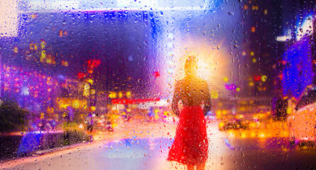 View through a glass window with raindrops on a blurred silhouette of a people under an umbrella...