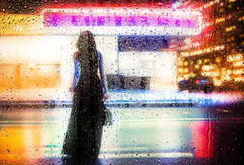 View through a glass window with raindrops on a blurred silhouette of a people under an umbrella walking on autumn rain , night street scene. focus on raindrops