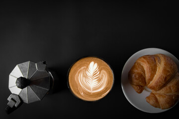 Latte art coffee in a white cup Two sides with Italian Moka pots, coffee and croissants, top view, black background, empty space, and three intersections for use.