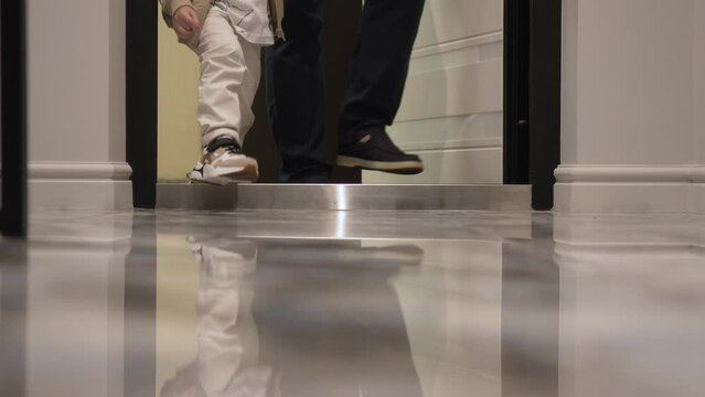 Dad and son came home after a walk. The legs of an adult man in brown sports shoes with white soles and the small legs of a boy in beige sneakers.