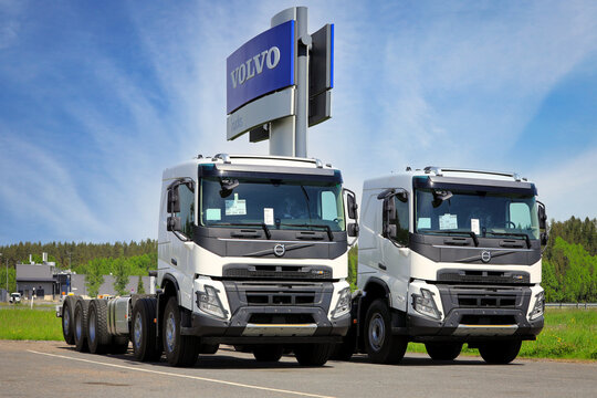 Two new, white Volvo FMX heavy duty trucks for construction parked on a yard under Volvo Trucks logo. 