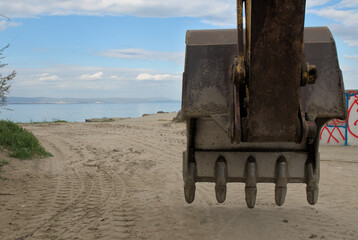 Fototapeta na wymiar Excavator bucket on the background of the beach and the sea