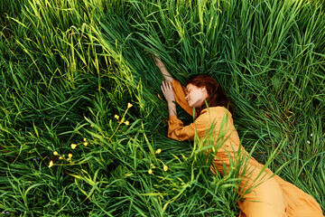 a relaxed woman enjoys summer lying in the tall green grass in a long orange dress stretched out stretching her arm forward