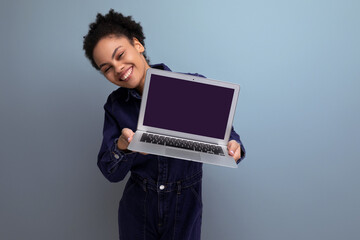 young successful woman with dark skin and black curly hair dressed in a blue denim suit demonstrates a project on a laptop screen
