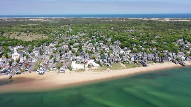 aerial video footage, flight along Cape Cod coastline at Provincetown, Massachusetts with houses along the beach, piers and boats in water and natural landscape in the background 
