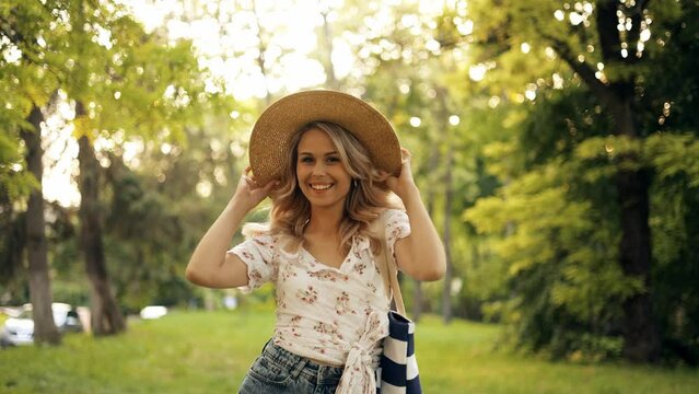 Open portrait of a beautiful smiling young woman in a straw hat walking in a green park feeling happiness on a summer sunny day during vacation, on the way to the beach