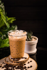 iced cappuccino coffee In a glass ready to serve Beautifully decorated with green leaves and coffee beans on a black background.