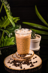 iced cappuccino coffee In a glass ready to serve Beautifully decorated with green leaves and coffee beans on a black background.