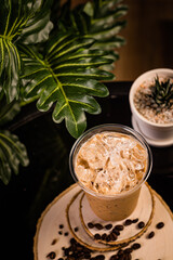 iced cappuccino coffee In a glass ready to serve Beautifully decorated with green leaves and coffee beans on a black background.