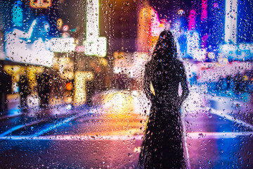 iew through glass window with rain drops on blurred reflection silhouette of a girl on a city...