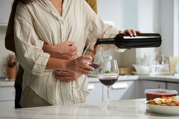Cropped image of man hugging girlfriend when she is pouring red wine in glasses