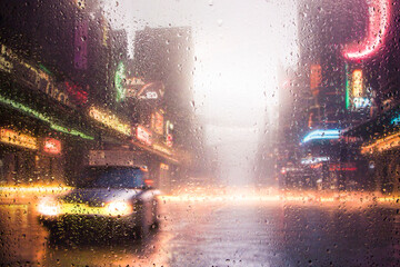 View through a glass window with raindrops on city streets with cars in the rain, bokeh of colorful city lights, night street scene. Focus on raindrops on glass