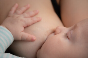 Newborn baby sucks mother's breast milk. Beautiful tranquil child peacefully sleeping while breastfeeding. Closeup portrait.