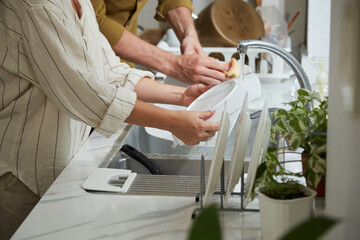 Fototapeta premium Cropped image of couple rinsing plates under tap water after having dinner at home