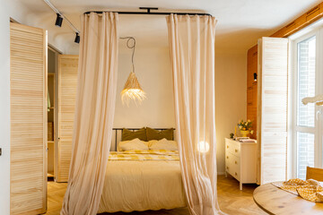 Fototapeta na wymiar Interior view of bedroom in beige tones with straw lampshade and wardrobe shutters. Boho style natural materials