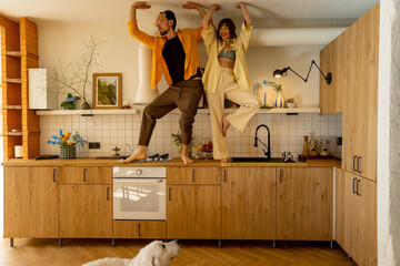 Young couple having fun, standing together on a kitchen table at their stylish and cozy apatment studio. Man and woman spends leisure time happily indoors