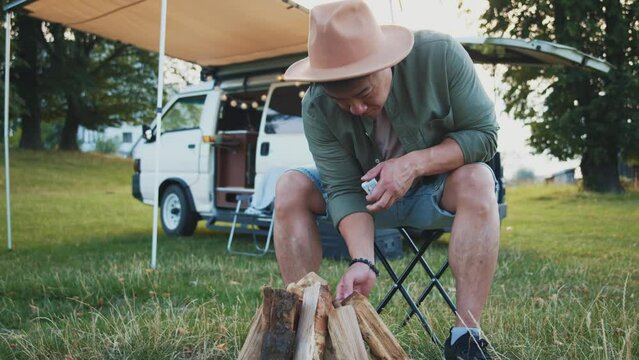 Man camping in summer. Campfire near camper van outdoors. Yuong asian
