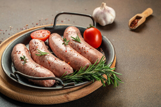 Raw sausages with herbs and spices on a light background. Food recipe background. Close up