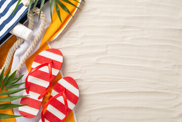 Enjoy the summer breeze. Top view of beach bag, flip-flops, sunscreen, towel, palm leaves, on sandy...